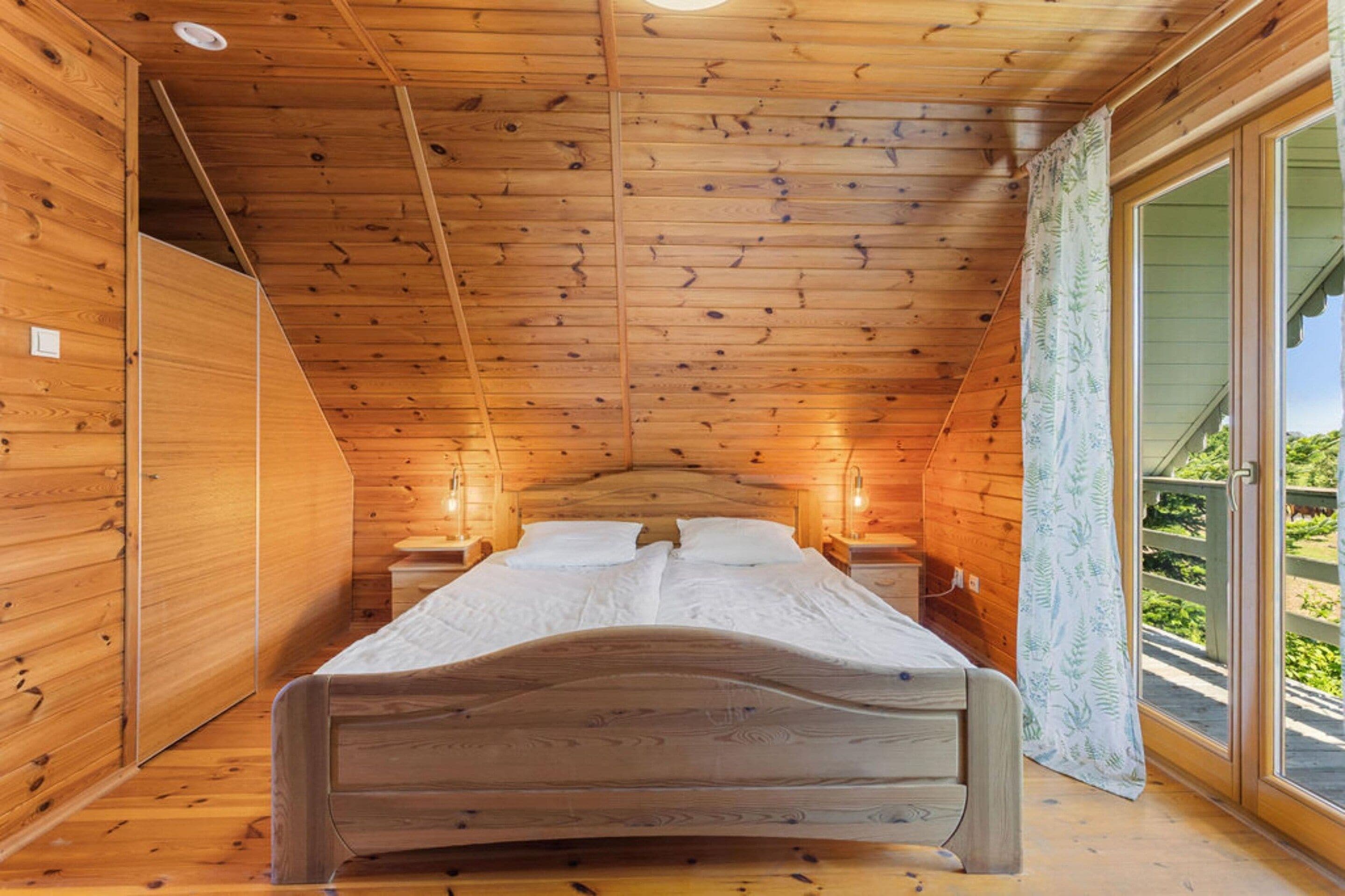 Un dormitorio de cabaña de madera con cama, lámparas de noche y vista a la vegetación.
