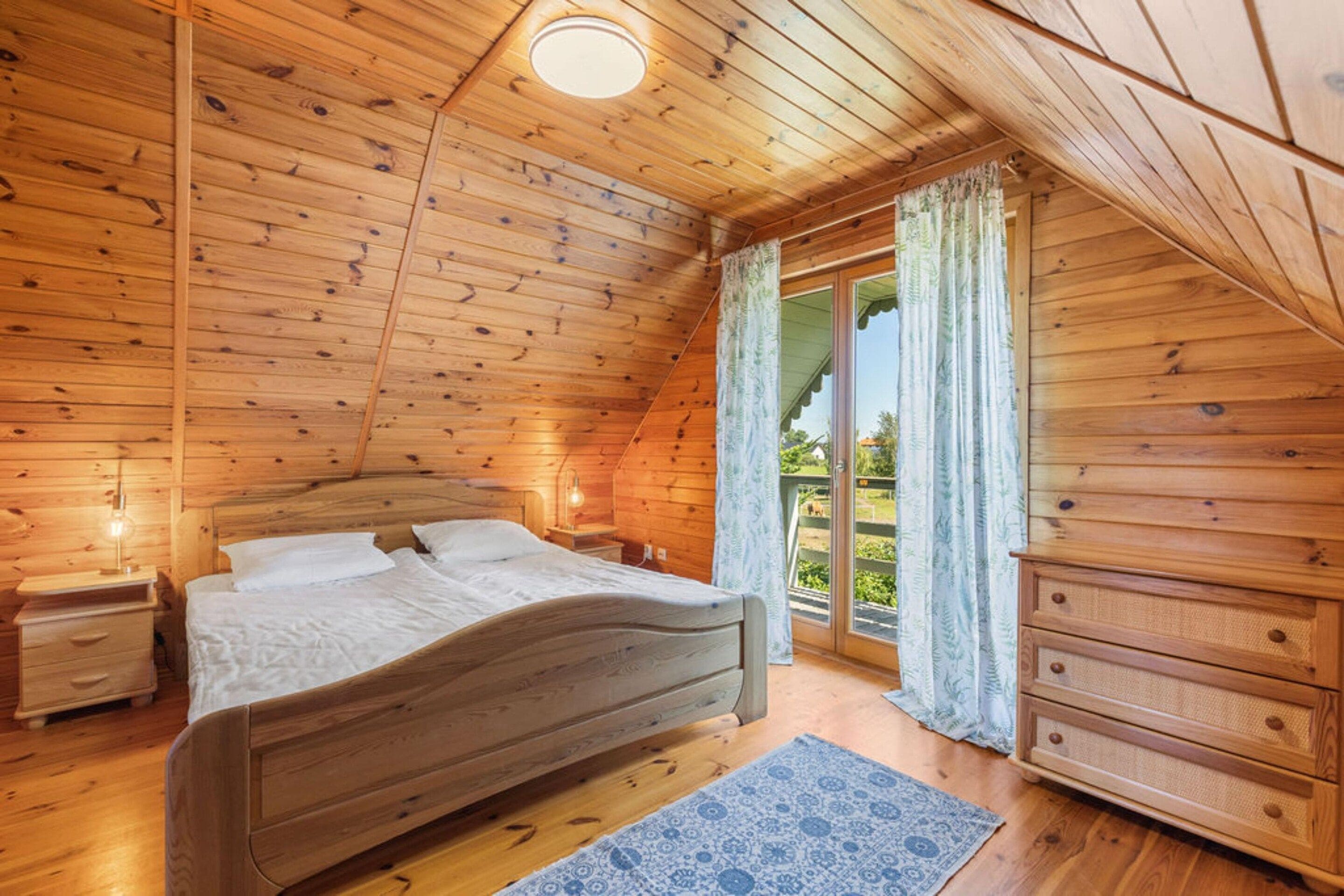 A wooden cabin bedroom with a bed, nightstands, a dresser, and a window with curtains.