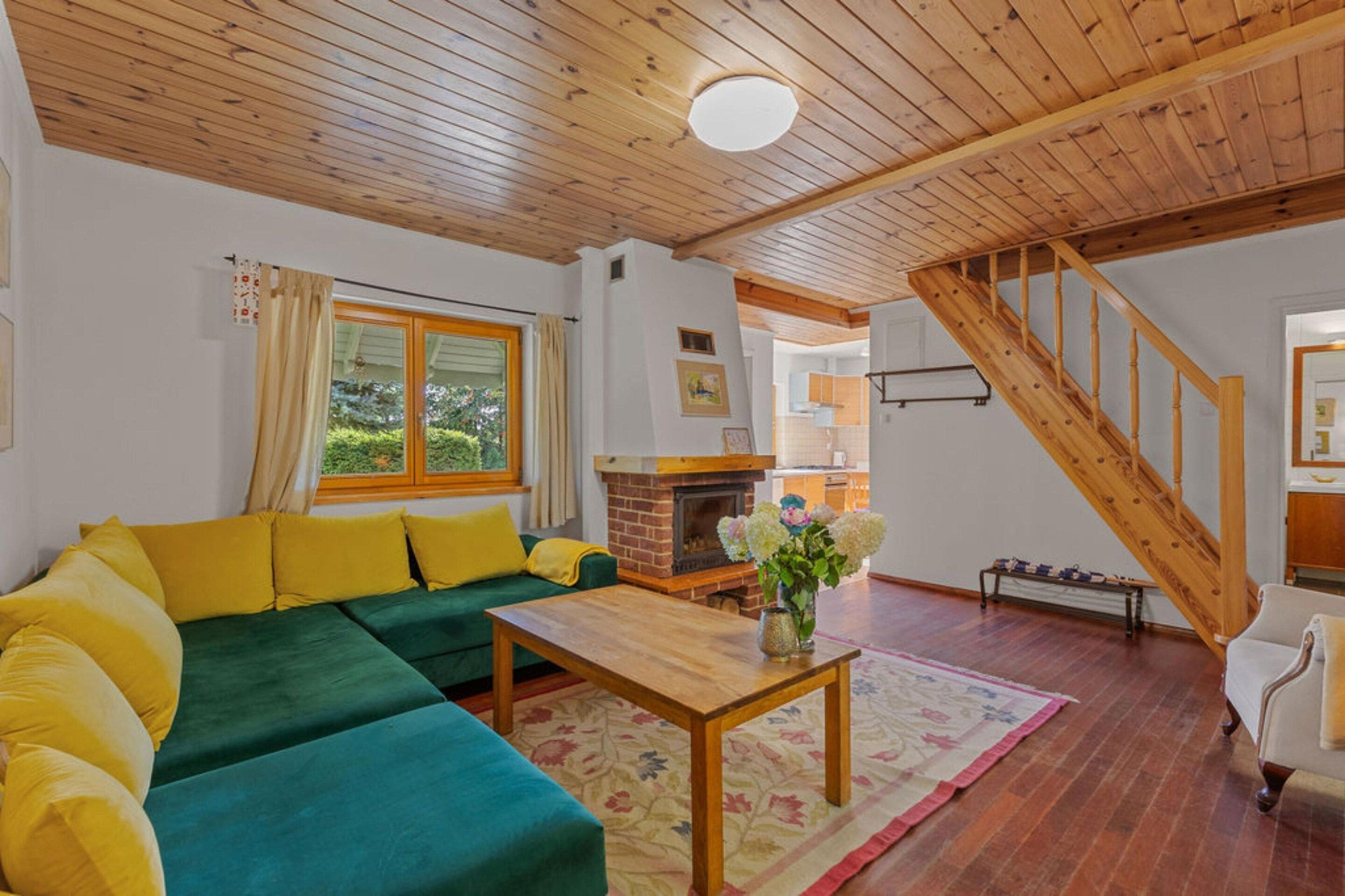 A cozy living room with a green sofa, wooden ceiling, and a fireplace.