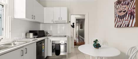 A modern kitchen with white cabinets, a stainless steel sink, and a small dining area with a white table and chairs.