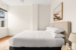 Ein Schlafzimmer mit Bett, Fenster, einem Bild und einem Nachttisch.