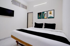 A bedroom with a bed, a flat-screen TV mounted on the wall, and three framed artworks above the bed.