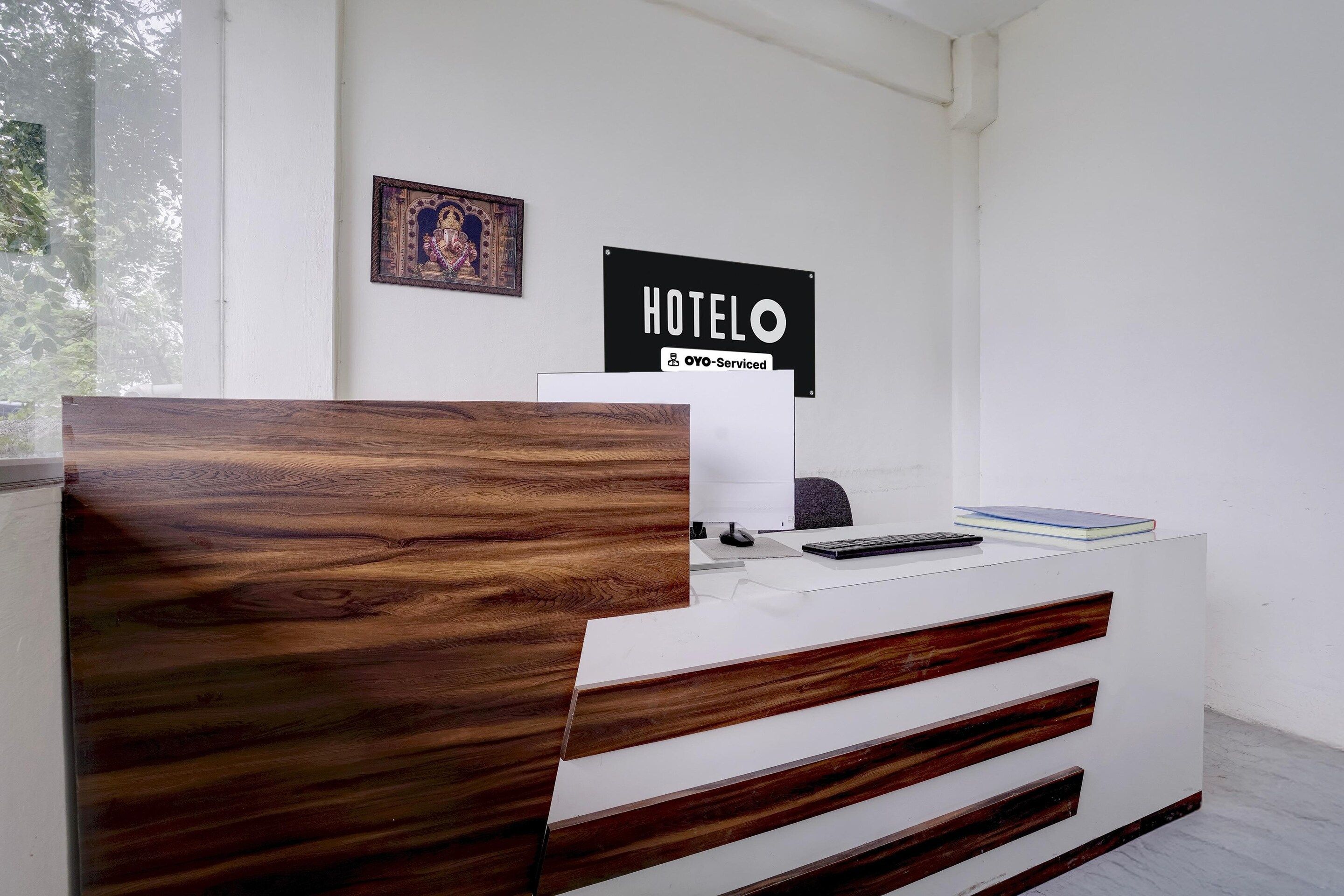 Un mostrador de recepción con panel frontal de madera, un letrero que dice 'HOTEL OYO-Serviced' y un cuadro enmarcado en la pared.