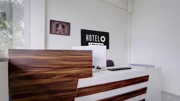 Un mostrador de recepción con panel frontal de madera, un letrero que dice 'HOTEL OYO-Serviced' y un cuadro enmarcado en la pared.