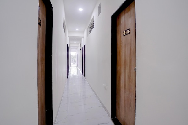 A corridor with wooden doors, white walls, and a tiled floor.