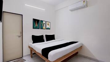 Un dormitorio con cama, puerta, equipo de aire acondicionado y tres cuadros en la pared.