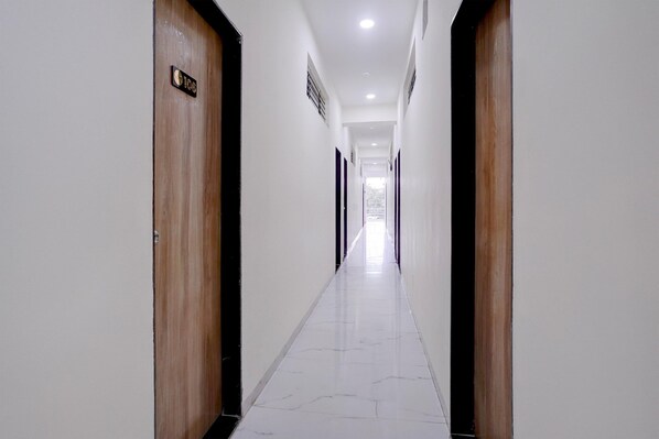 A long, narrow hallway with wooden doors on either side and a tiled floor. - Hotel O Bamu University (Chhatrapati Sambhajinagar)