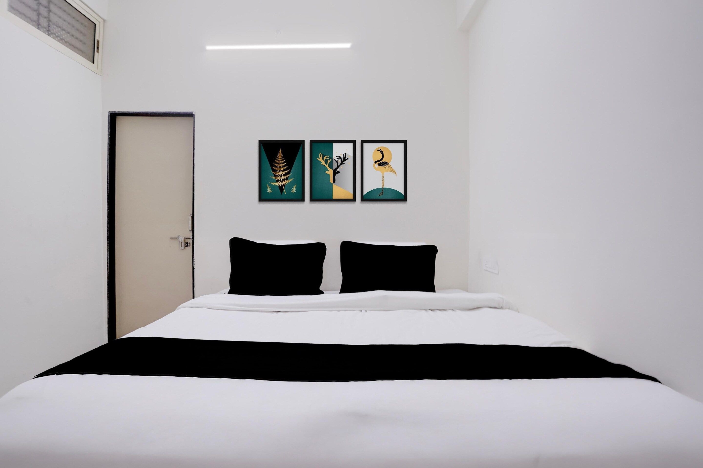 Una habitación de hotel con una cama, dos almohadas negras y tres obras de arte enmarcadas en la pared.