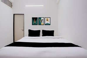 Una habitación de hotel con una cama, dos almohadas negras y tres obras de arte enmarcadas en la pared.