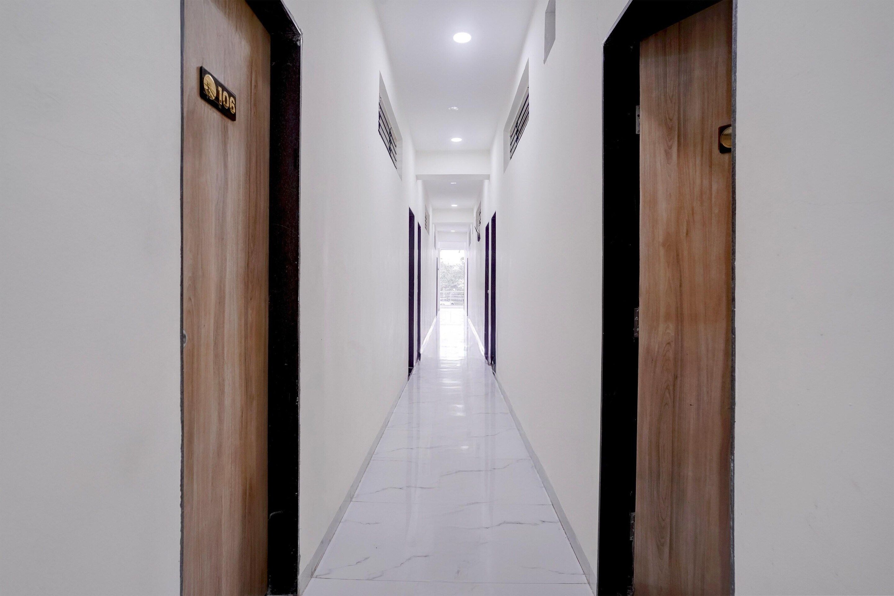 Un pasillo largo y estrecho con puertas de madera a ambos lados, que conduce a una habitación luminosa al final.