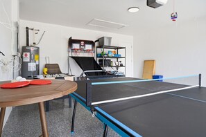 Uma mesa de tênis de mesa com uma rede, um aro de basquete e uma estante com diversos objetos.