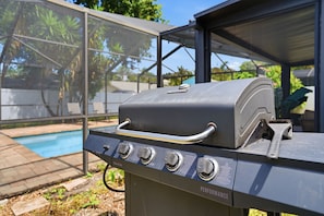 A barbecue grill with a digital display, positioned outdoors with a view of a swimming pool and greenery in the background. - Peaceful 3-bedroom house with AC in charming Largo (Largo)