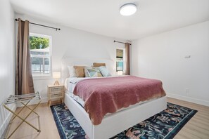 A bedroom with a bed, a nightstand, a lamp, a window with curtains, and a wooden floor. - Peaceful 3-bedroom house with AC in charming Largo (Largo)