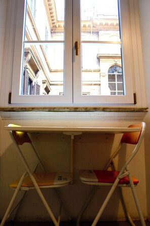 Ein Fenster mit Blick auf eine Gebäudefassade, eine weiße Tür und ein kleiner Tisch mit zwei Stühlen darunter.