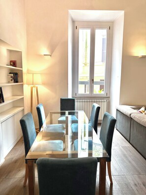 A modern dining area with a glass-top table, blue upholstered chairs, a floor lamp, and a sofa. - Luxury Residence in Central Rome by Spanish Steps (Roma)