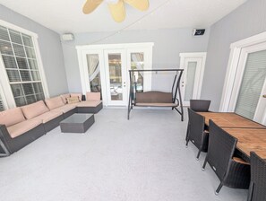 A covered patio area with a sectional sofa, a swing, and a dining table with chairs. - Monterey Bay Retreat | Private Pool + Gated (Jacksonville)