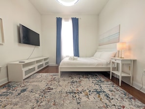 A bedroom with a bed, a TV, a bedside table with a lamp, and a window with curtains. - Monterey Bay Retreat | Private Pool + Gated (Jacksonville)