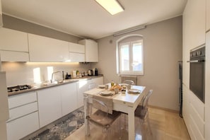 Eine moderne Küche mit weißen Schränken, einem Esstisch für vier Personen und einem eingebauten Backofen.