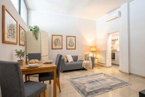 Ein modernes Wohnzimmer mit Esstisch, grauem Sofa und einer Lampe.