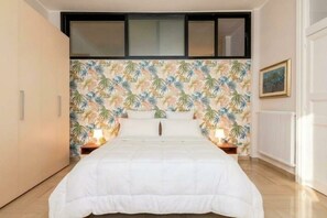 Ein Schlafzimmer mit Bett, Nachttisch, Fenster und Heizkörper.