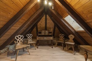 Een houten zolderkamer met een schuine kap, een klein tafeltje en vier stoelen met houtsnijwerk.