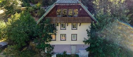 Ein zweistöckiges Haus mit geneigtem Dach, umgeben von üppigem Grün.