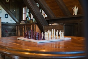 Een schaakbord op een ronde houten tafel in een kamer met houten balken en een klok aan de muur.