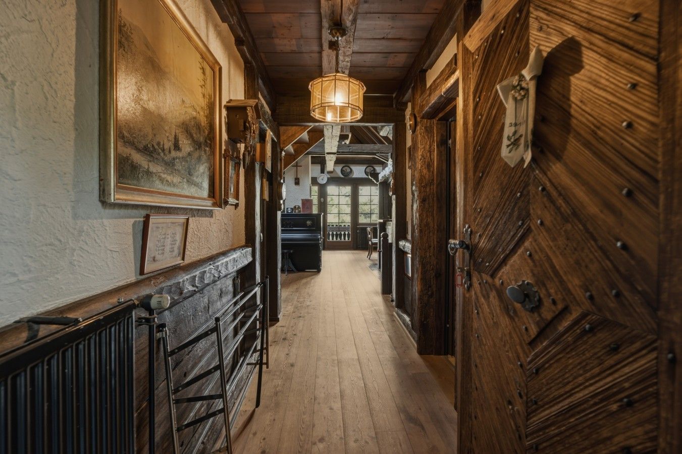 Un pasillo de madera con un radiador, una lámpara colgante y una puerta con placa decorativa.