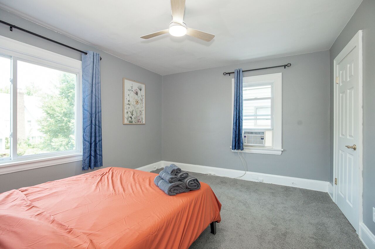 A bedroom with a bed, a ceiling fan, a window with curtains, and a door.
