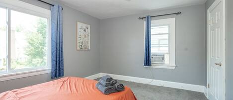 A bedroom with a bed, a ceiling fan, a window with curtains, and a door.