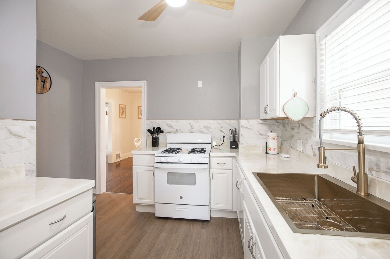 A kitchen with white cabinets, a white stove, a marble countertop, and a stainless steel sink.