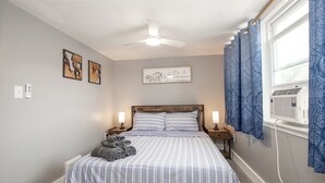 A bedroom with a bed, nightstands, a ceiling fan, a window with curtains, and wall art. - Spacious house in University heights (University Heights)