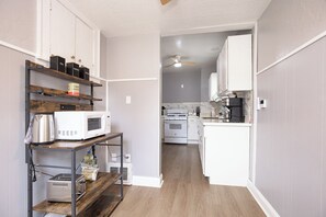 Eine kleine Küche mit weißen Schränken, einer Mikrowelle, einem Toaster und einer Kaffeemaschine auf einem Regal.