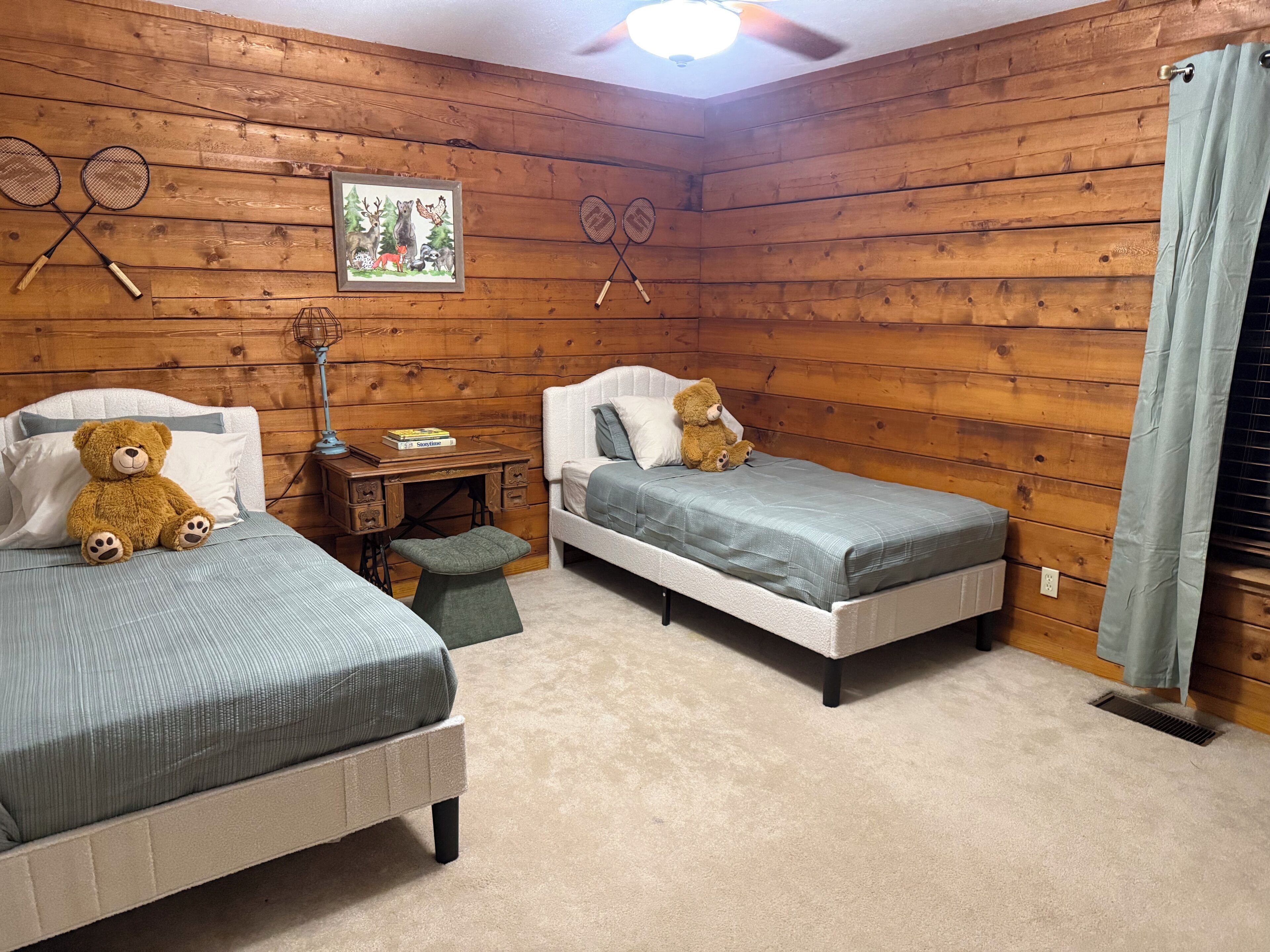 A room with two beds, a desk, a chair, a teddy bear, and a ceiling fan.