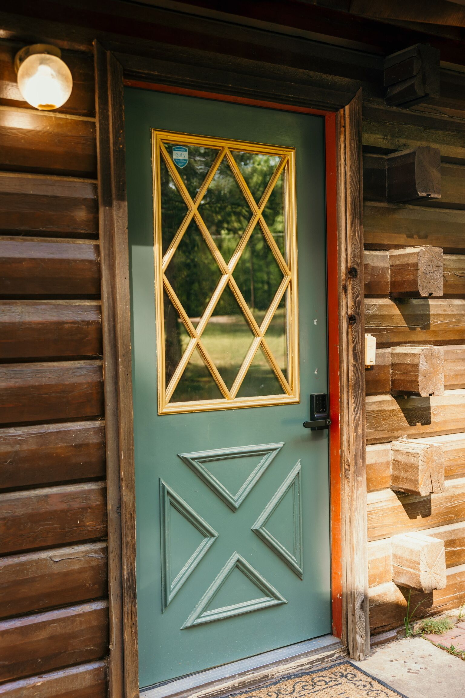 Una baita di legno con una porta verde, una finestra a motivi a diamante e un disegno geometrico sotto.