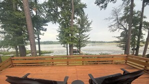 A wooden deck with two Adirondack chairs and a small table, overlooking a lake with a dock and a boat. - Charming 3-bedroom cabin with AC on Lone Star Lake (Lone Star)