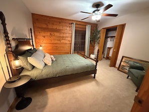 Ein Schlafzimmer mit Holz-Kopfteil, einem Bett mit grüner Bettdecke, einer Nachttischlampe und einem Deckenventilator.
