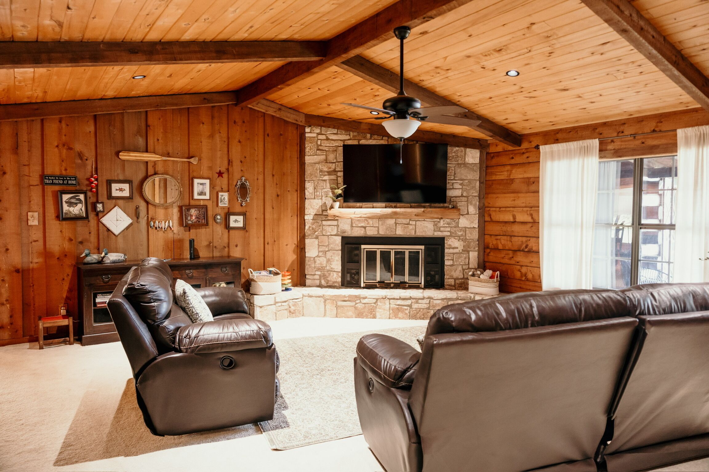 Interior de una cabaña de troncos con chimenea de piedra, sofás de cuero y un televisor montado.