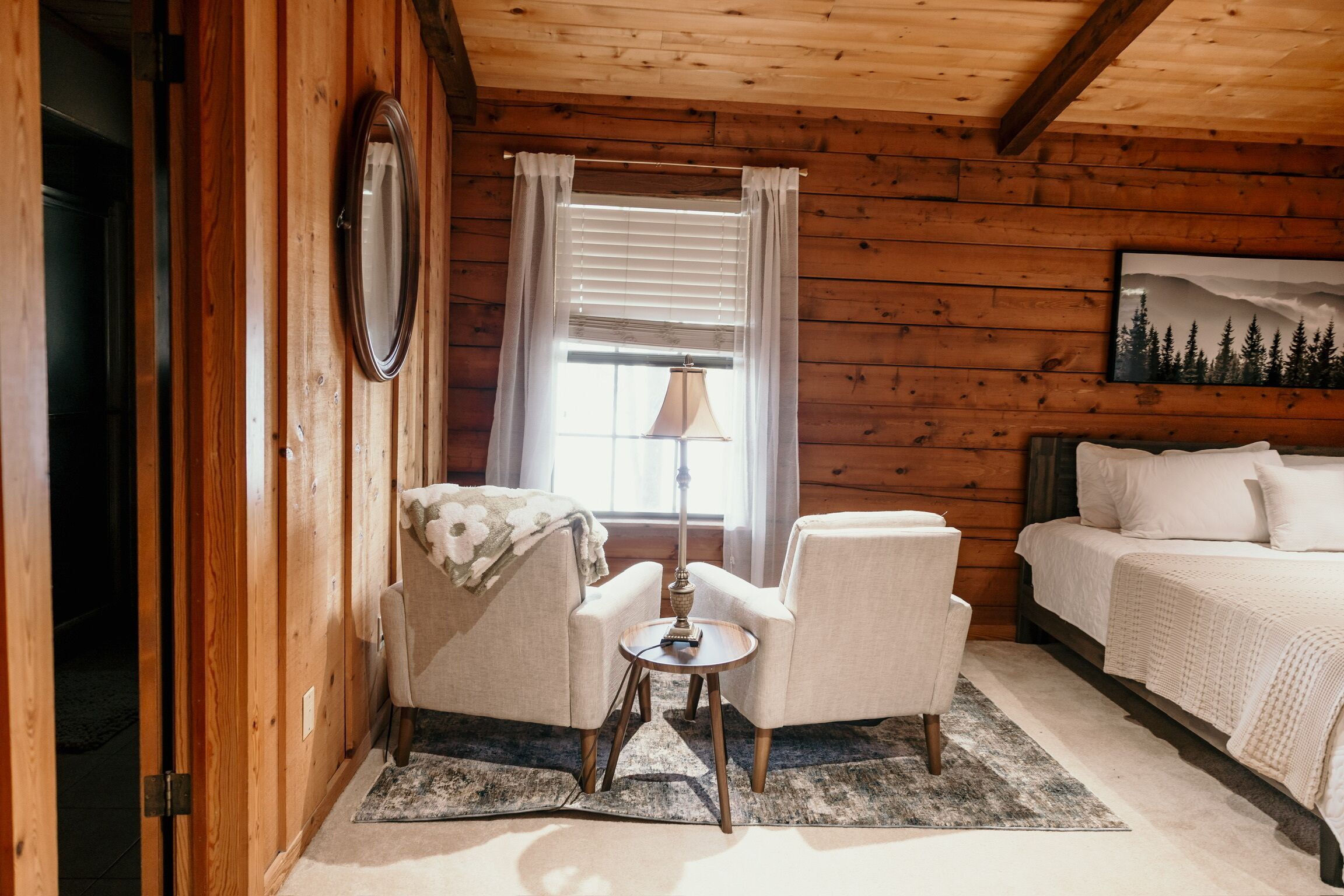 A cozy room with a bed, two armchairs, a small table, and a window with curtains.