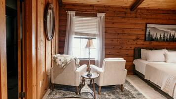 A cozy room with a bed, two armchairs, a small table, and a window with curtains.