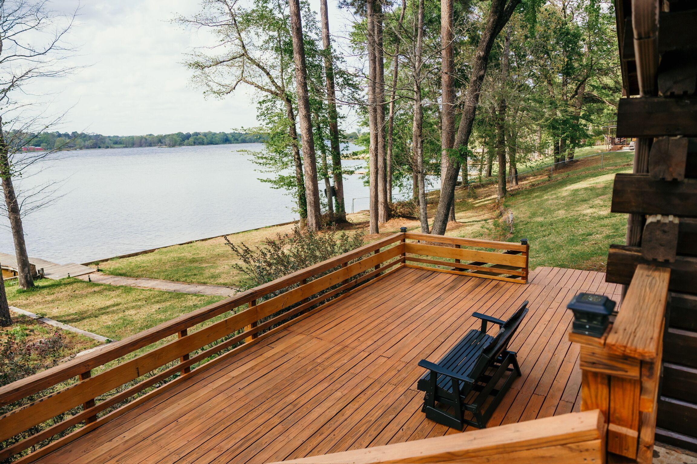 Un pontile in legno con una panchina e un tavolo, affacciato su un lago sullo sfondo con alberi.