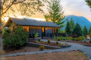 A cabin with a porch, surrounded by a landscaped garden and a mountain backdrop.