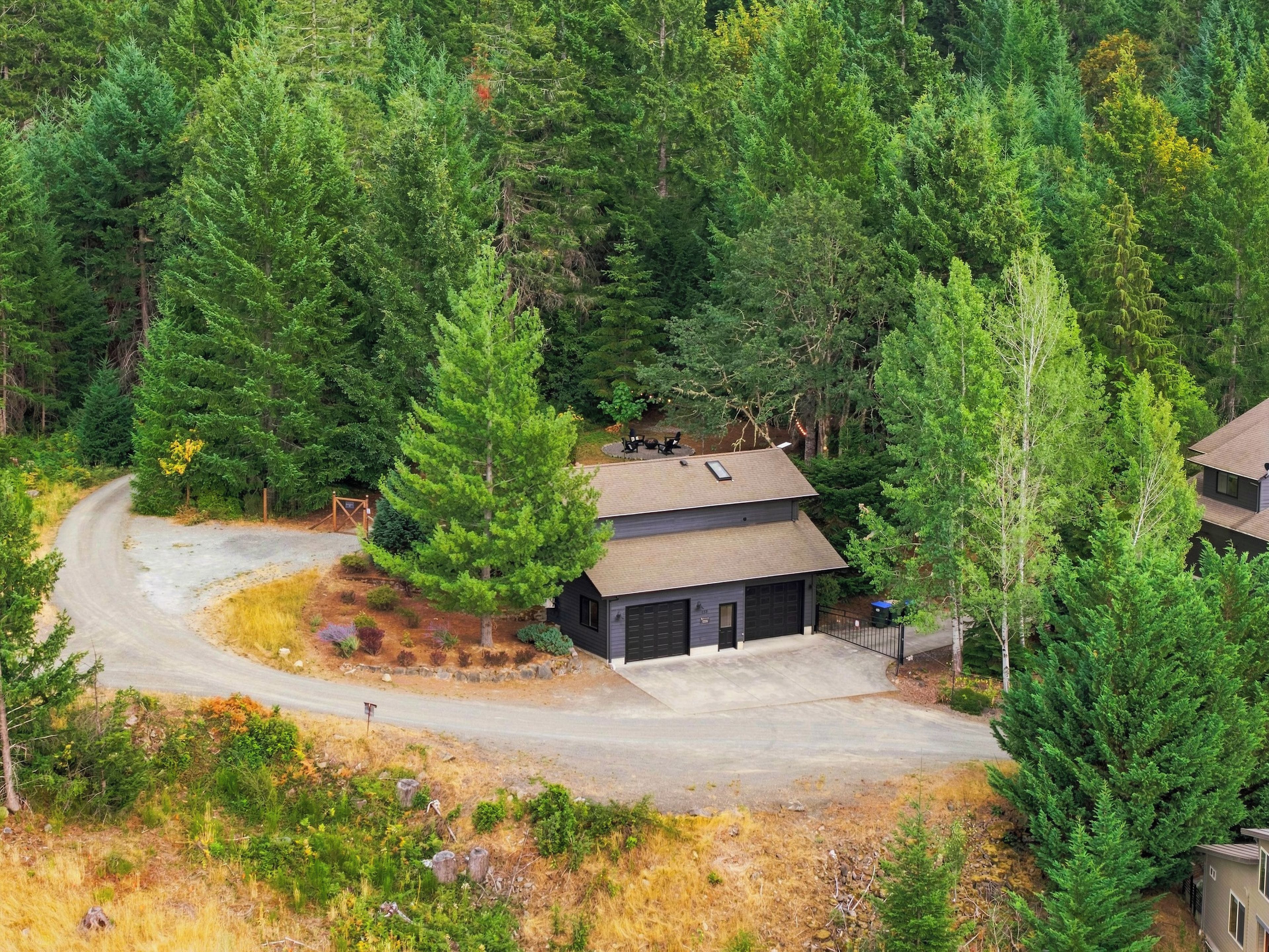 Une cabane à deux étages, entourée d’une forêt dense, avec une allée sinueuse menant à l’entrée.