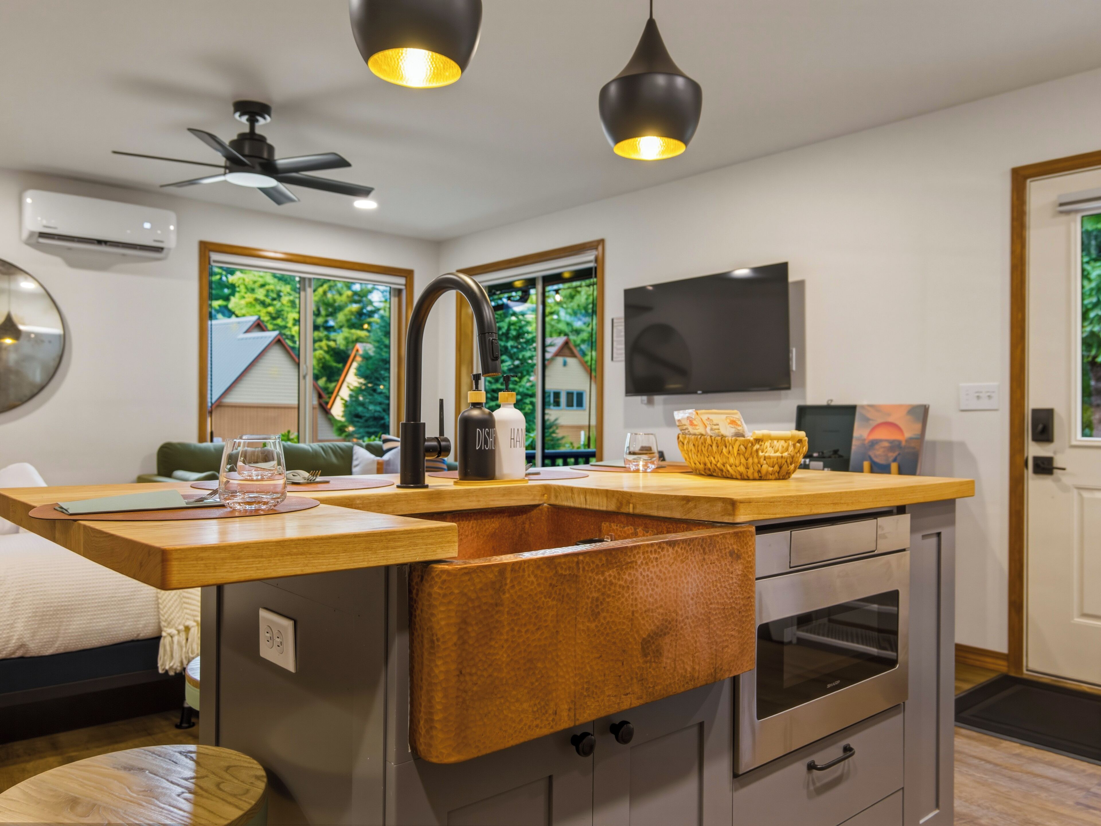 A modern kitchen with a built-in sink, a ceiling fan, and a flat-screen TV.