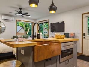 A modern kitchen with a built-in sink, a ceiling fan, and a flat-screen TV.
