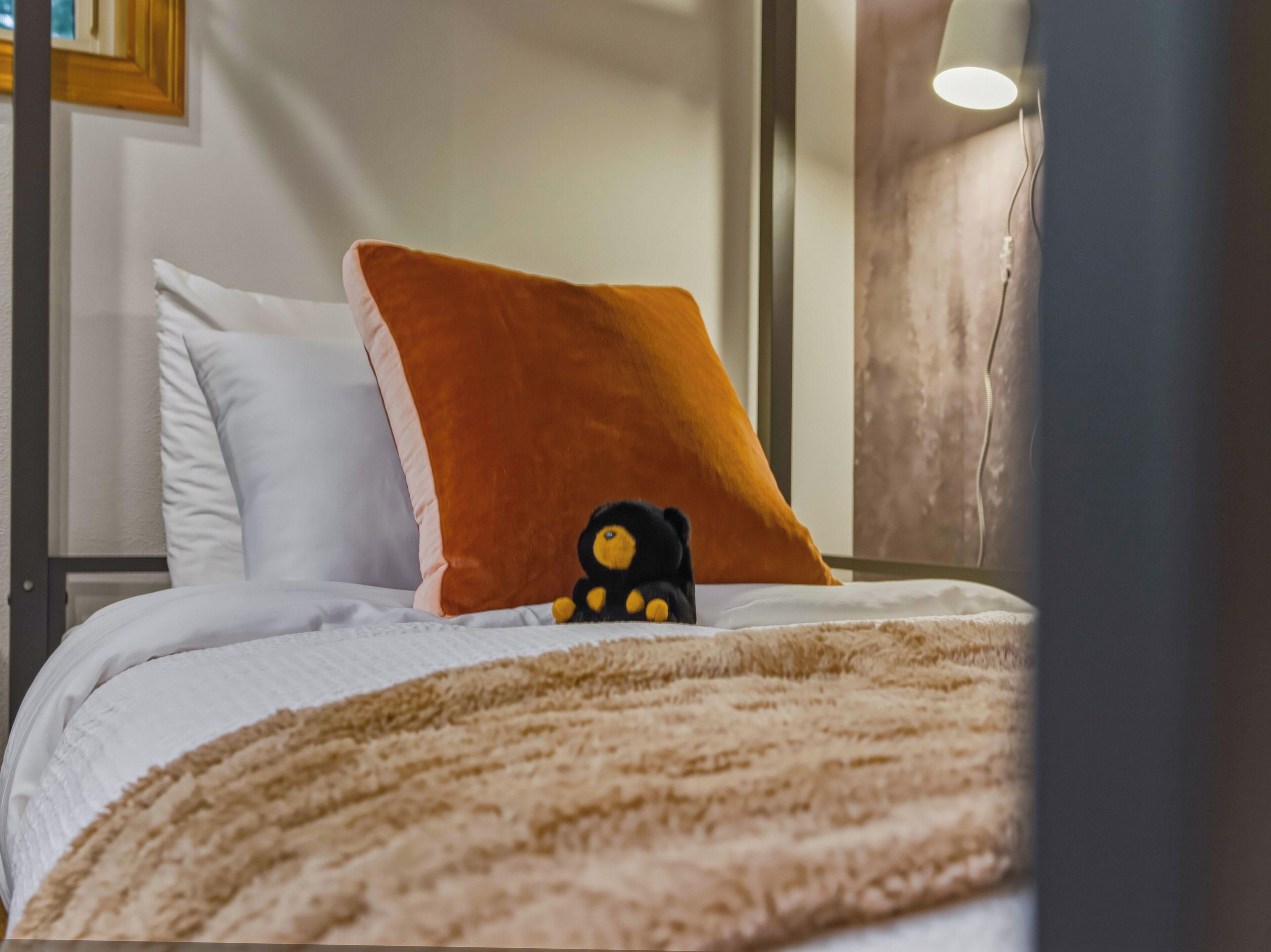 Un lit avec un oreiller blanc, un oreiller orange et un ours en peluche.