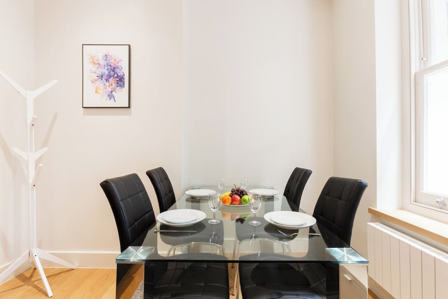 A dining area with a glass table, four chairs, and a fruit bowl.