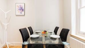 Un comedor con una mesa de vidrio, cuatro sillas y un frutero.