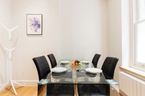 A dining area with a glass table, four chairs, and a fruit bowl. - Super Central Lovely 1BR Flat - Fitzrovia (London)