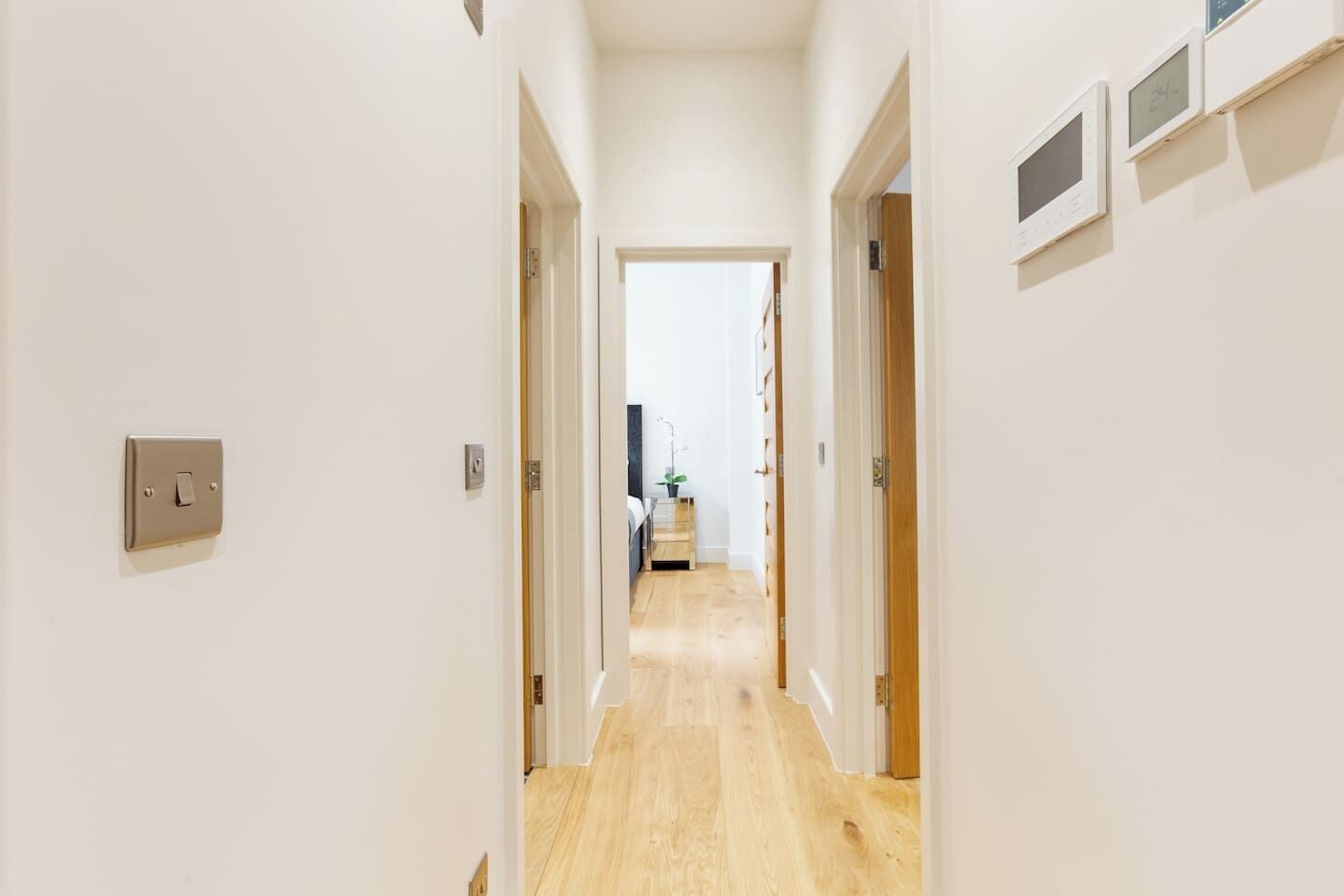 A narrow hallway with wooden flooring, white walls, and a door leading to a bedroom.